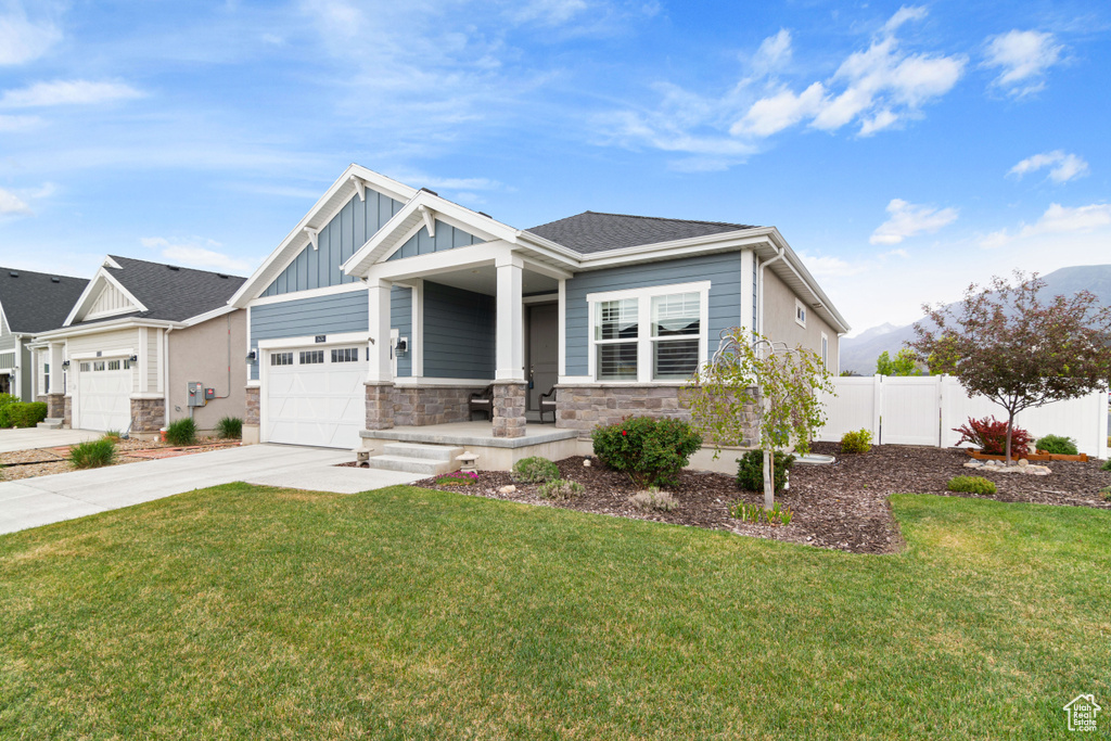 Craftsman-style home with board and batten siding, driveway, stone siding, covered porch, and a garage
