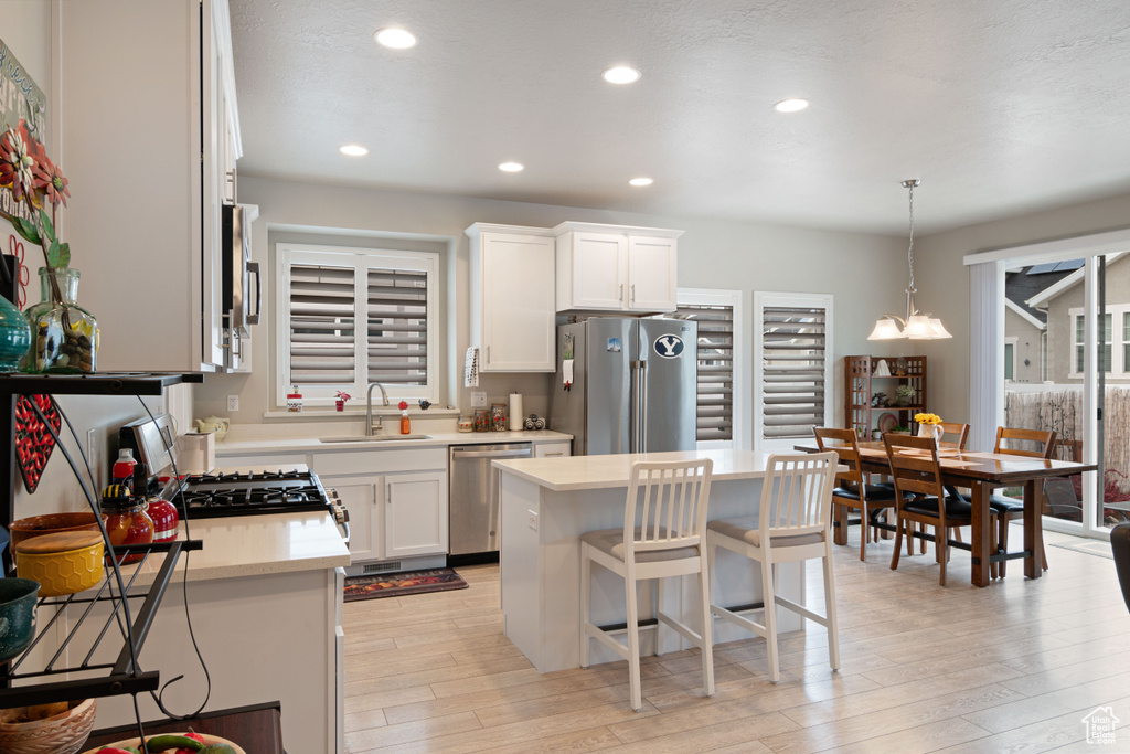 Kitchen with appliances with stainless steel finishes, a sink, light countertops, light wood finished floors, and white cabinetry