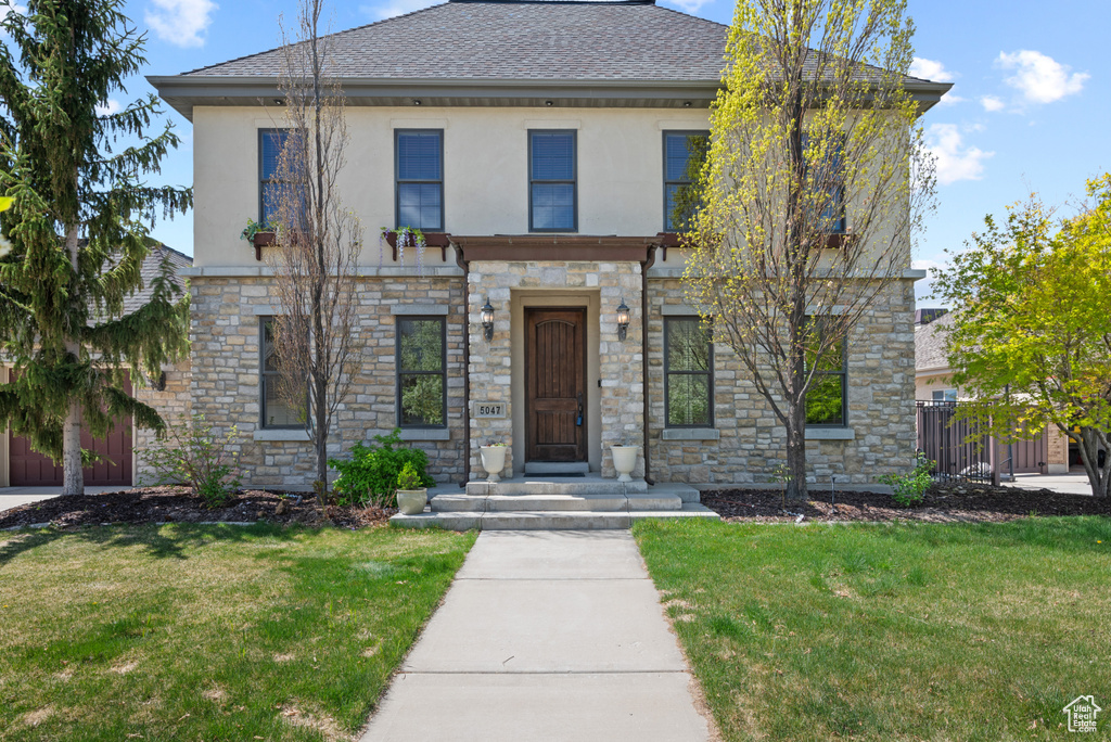 View of front of property featuring fence, stucco siding, a front lawn, and stone siding