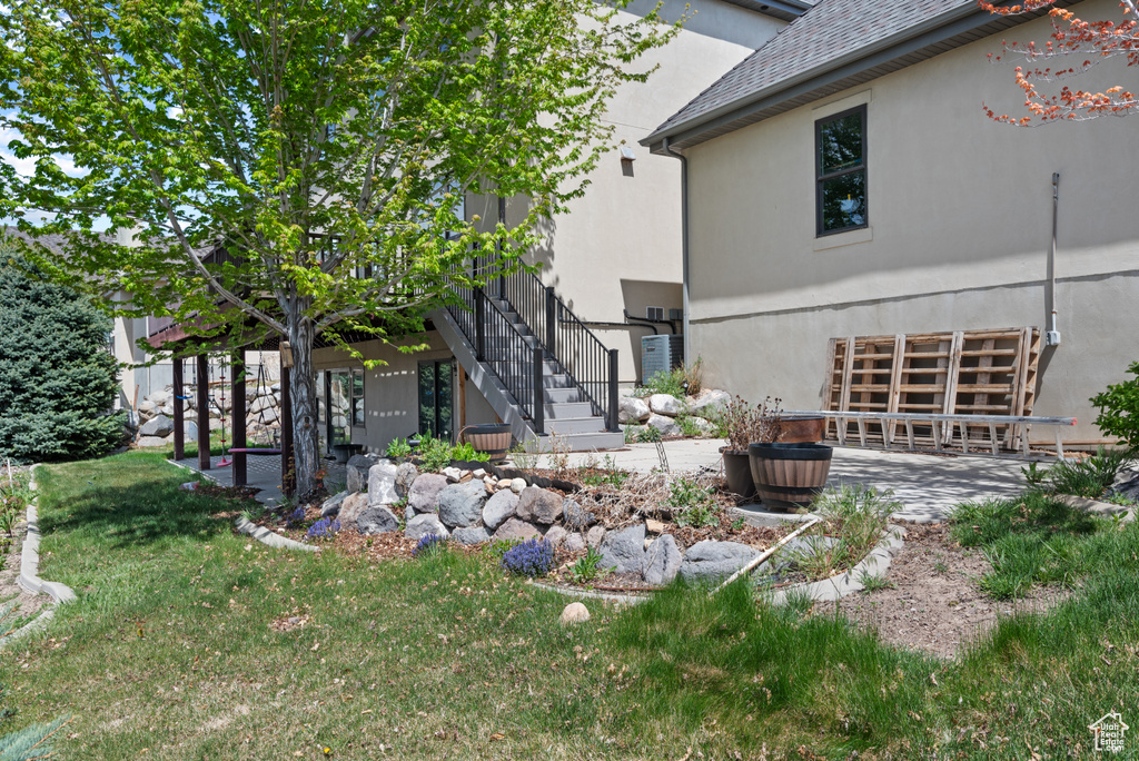 View of side of home with a lawn, a patio, an attached garage, stucco siding, and stairway