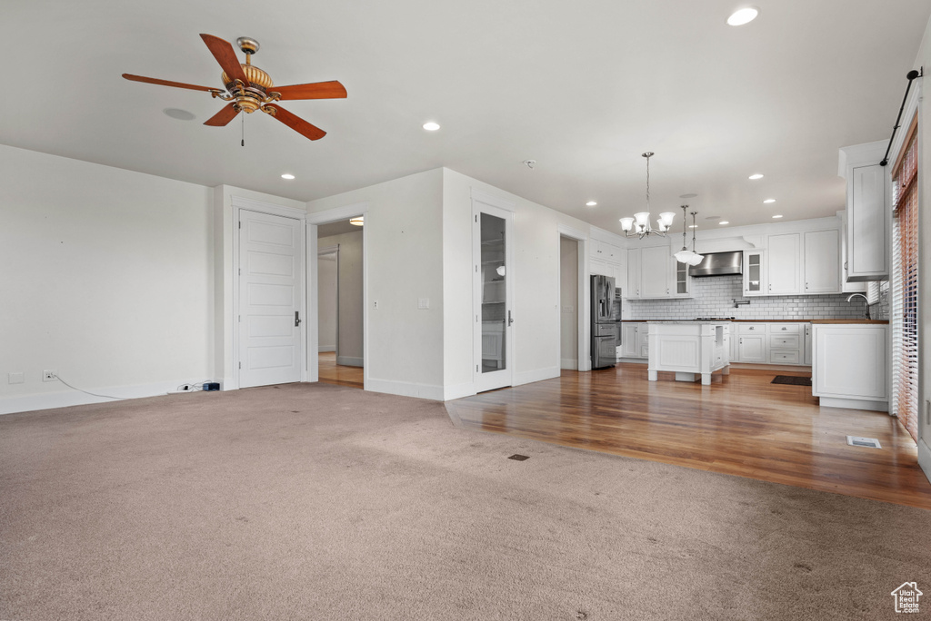 Unfurnished living room with ceiling fan with notable chandelier, a sink, baseboards, light carpet, and recessed lighting