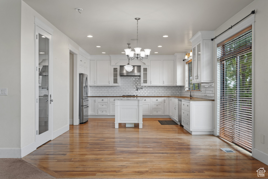 Kitchen featuring backsplash, a notable chandelier, appliances with stainless steel finishes, and wall chimney exhaust hood