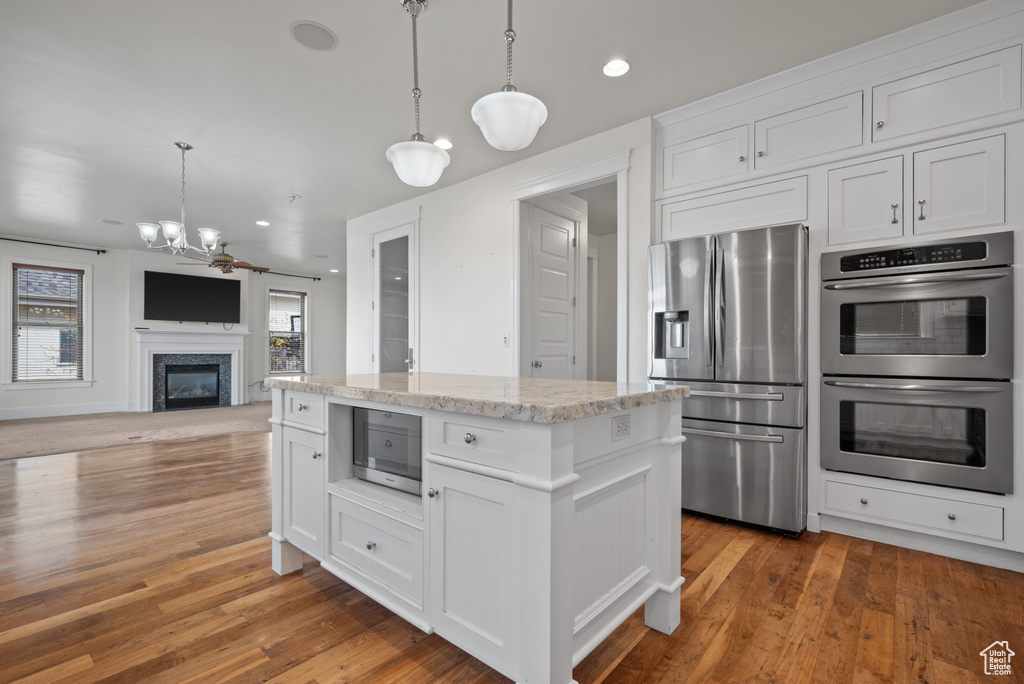 Kitchen with stainless steel appliances, wood finished floors, pendant lighting, an inviting chandelier, and white cabinets