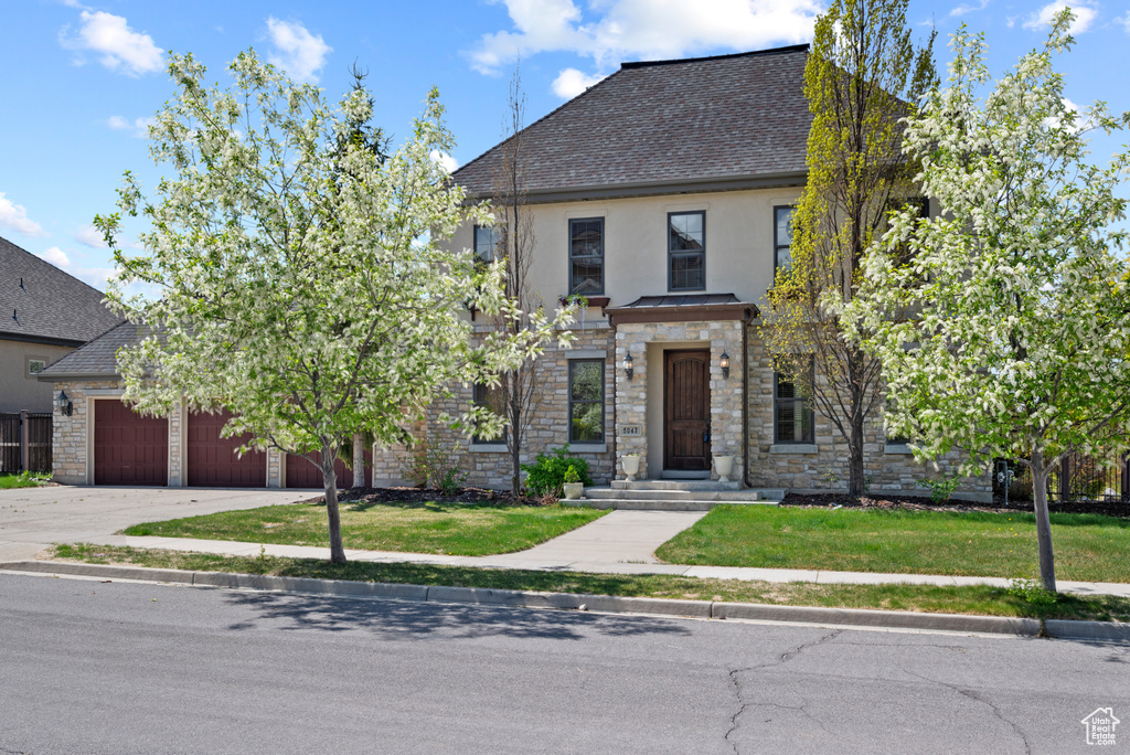 View of front of home featuring driveway, an attached garage, stucco siding, stone siding, and roof with shingles