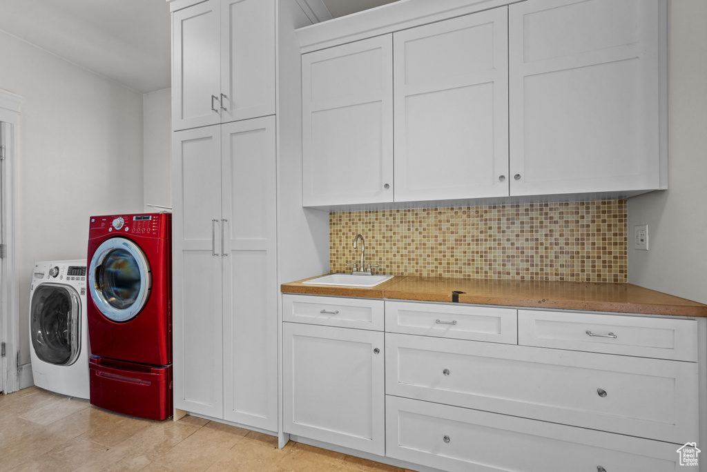 Washroom featuring cabinet space, washing machine and dryer, wet bar, and a sink