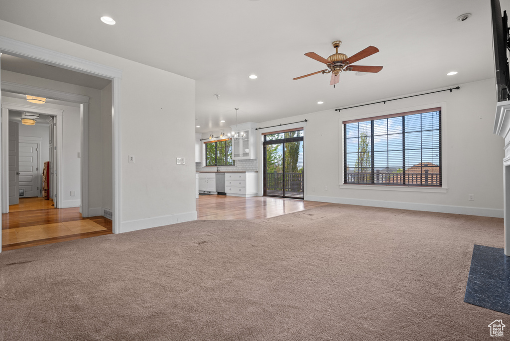 Unfurnished living room with light colored carpet, baseboards, ceiling fan with notable chandelier, and recessed lighting