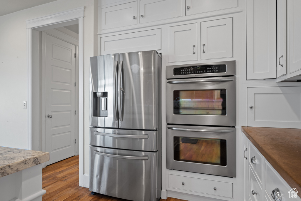Kitchen with stainless steel appliances, white cabinetry, and wood finished floors
