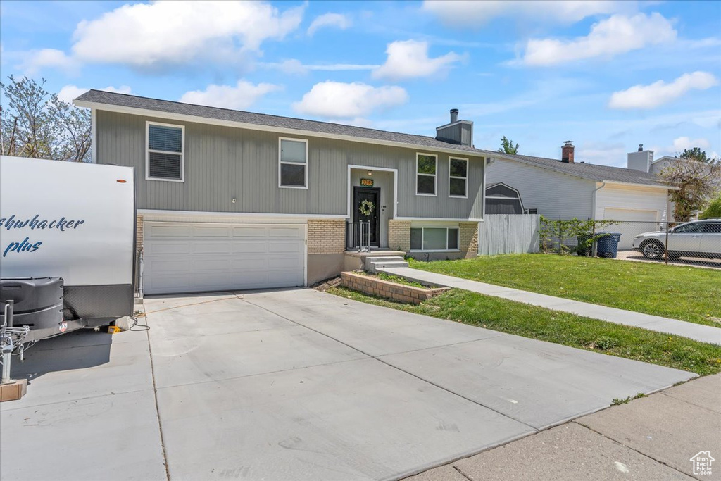 Raised ranch featuring brick siding, concrete driveway, a garage, a front lawn, and a chimney