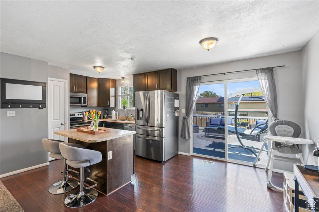 Kitchen with a center island, dark brown cabinets, a sink, stainless steel appliances, and dark wood-style floors