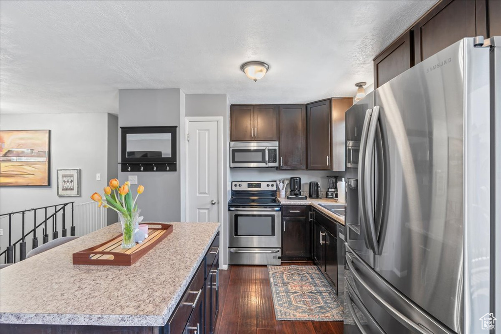 Kitchen featuring a center island, dark brown cabinetry, light countertops, appliances with stainless steel finishes, and dark wood-style floors