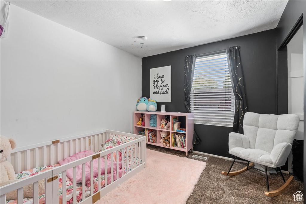 Carpeted bedroom with a crib and a textured ceiling