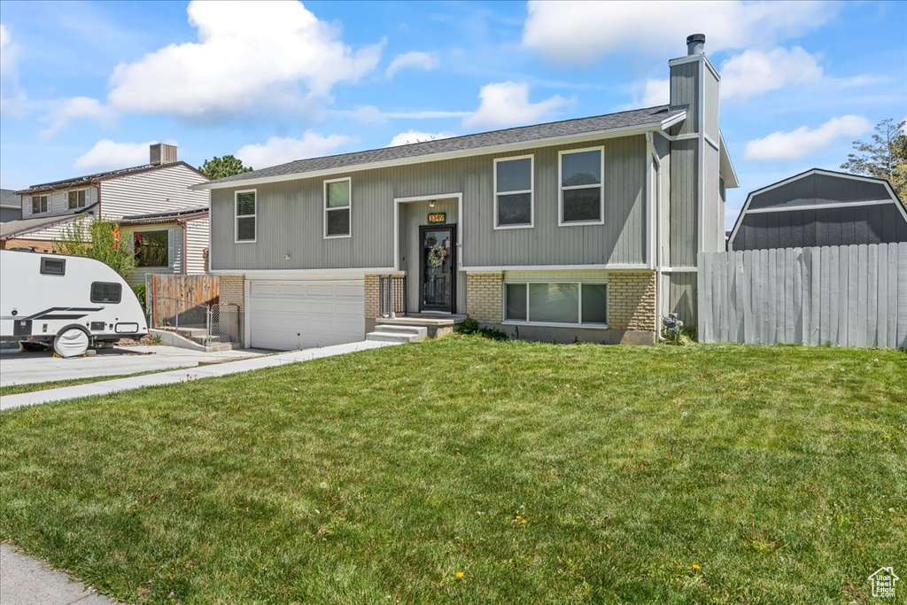 Split foyer home featuring a garage, a chimney, fence, a front lawn, and brick siding