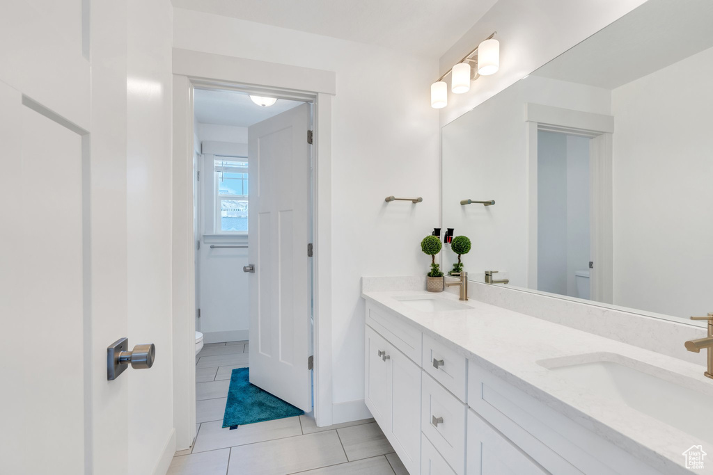 Full bath featuring toilet, tile patterned flooring, double vanity, and a sink