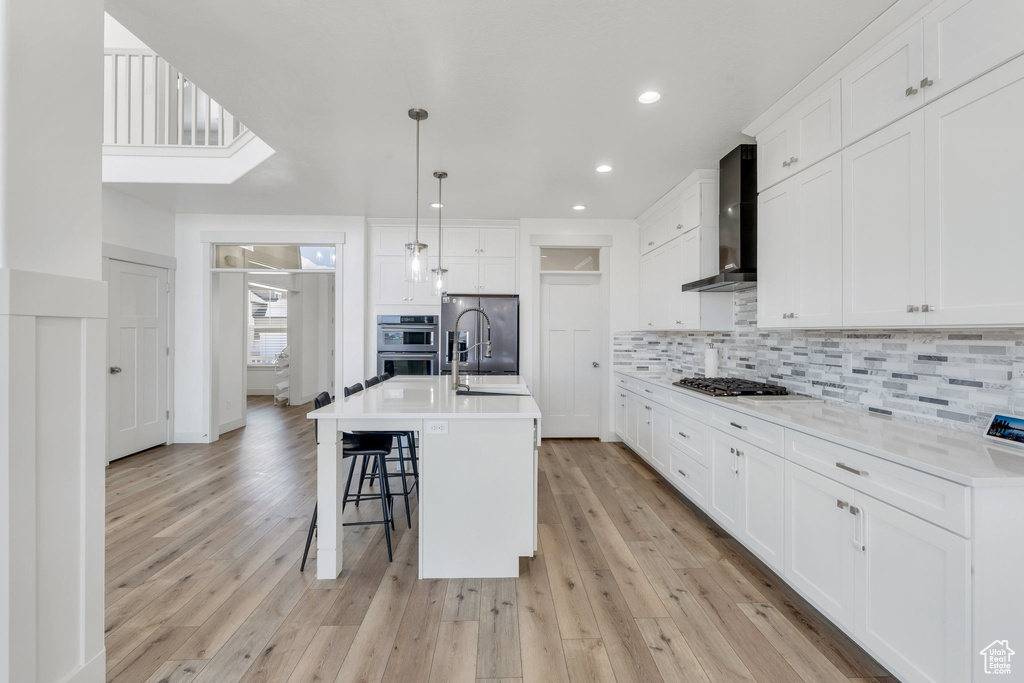 Kitchen with a breakfast bar area, backsplash, wall chimney range hood, white cabinets, and appliances with stainless steel finishes
