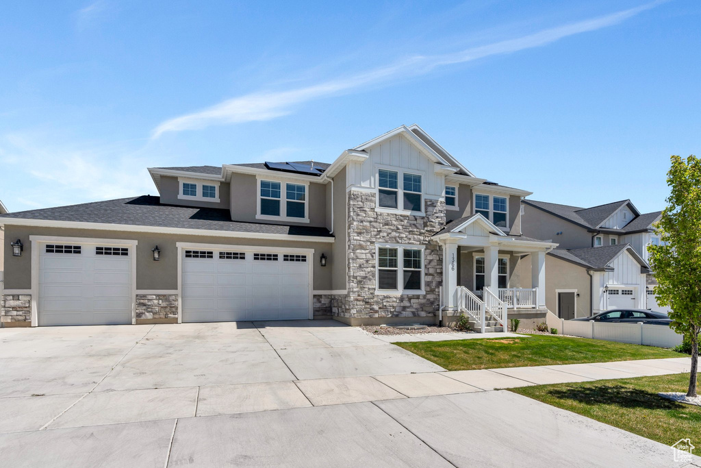 Craftsman house featuring stone siding, concrete driveway, roof mounted solar panels, and board and batten siding