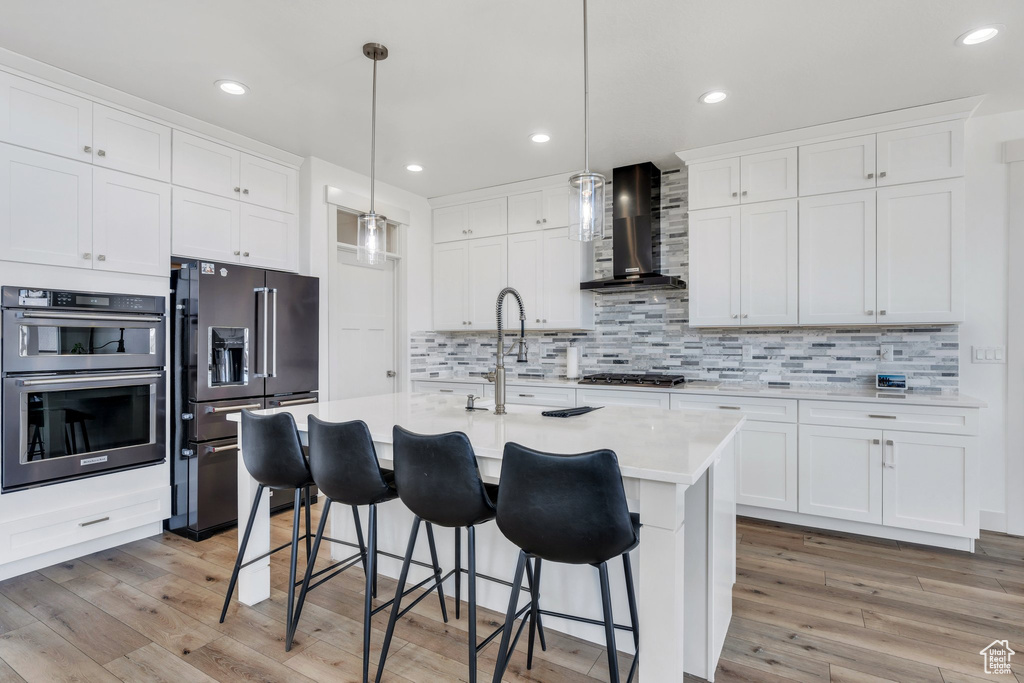 Kitchen featuring light countertops, wall chimney exhaust hood, appliances with stainless steel finishes, and light wood-type flooring