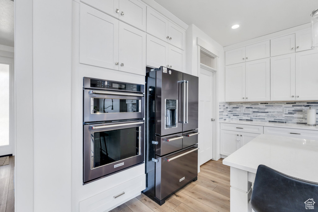 Kitchen with stainless steel appliances, recessed lighting, light countertops, white cabinets, and light wood-style floors