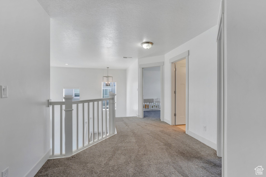 Corridor with light colored carpet, a textured ceiling, an upstairs landing, a chandelier, and baseboards