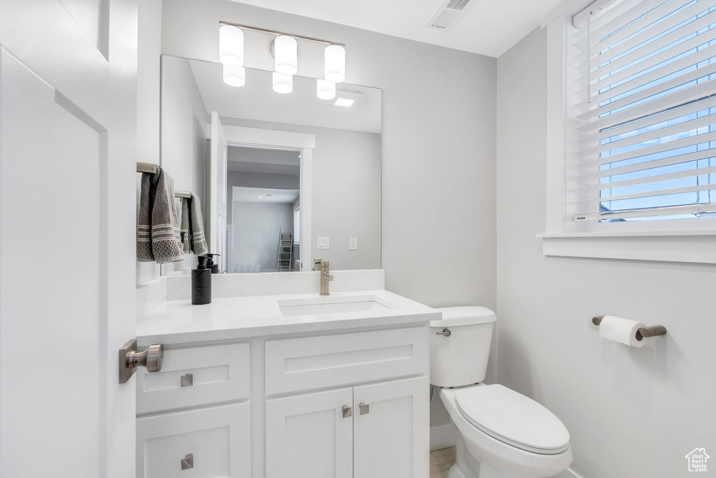 Half bathroom with vanity, toilet, baseboards, and visible vents