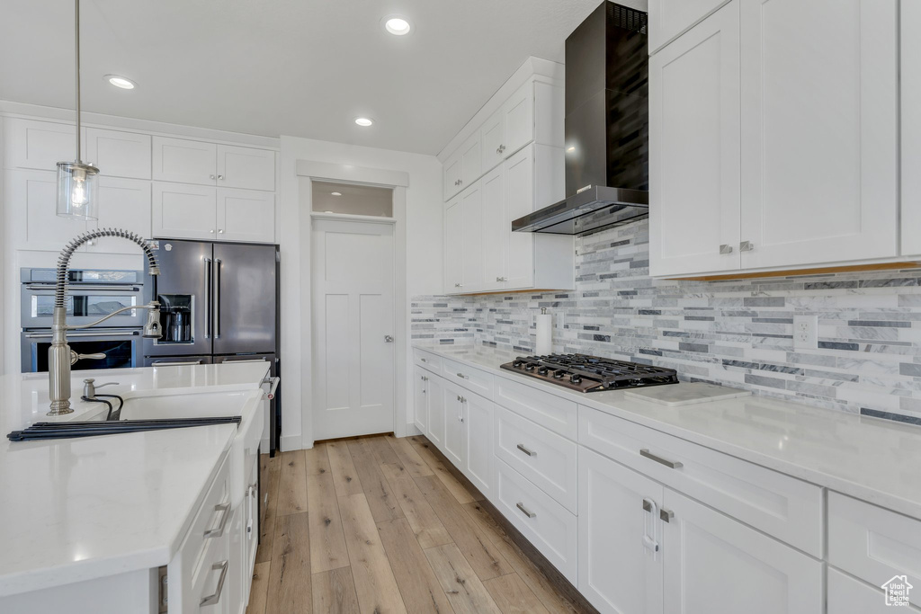Kitchen featuring stainless steel appliances, wall chimney range hood, light wood-type flooring, recessed lighting, and white cabinetry
