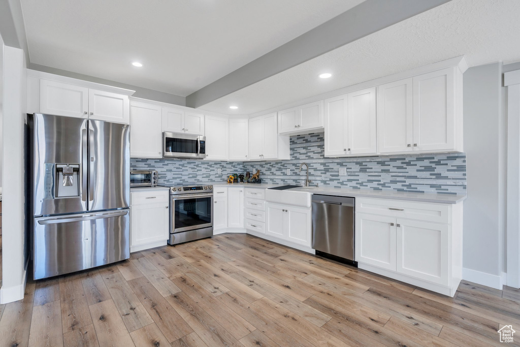 Kitchen with a sink, stainless steel appliances, white cabinetry, and light wood-style floors