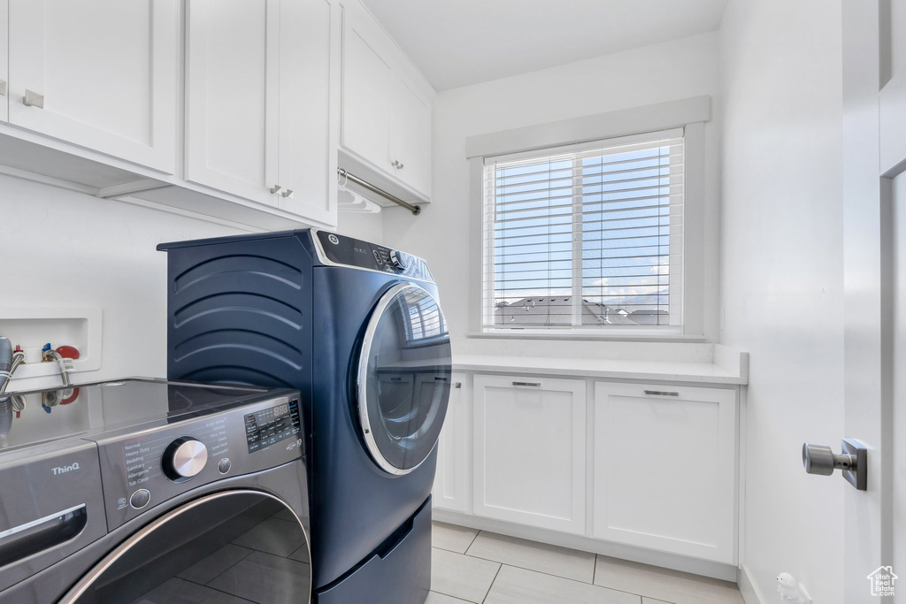Washroom with cabinet space, washing machine and clothes dryer, and light tile patterned flooring