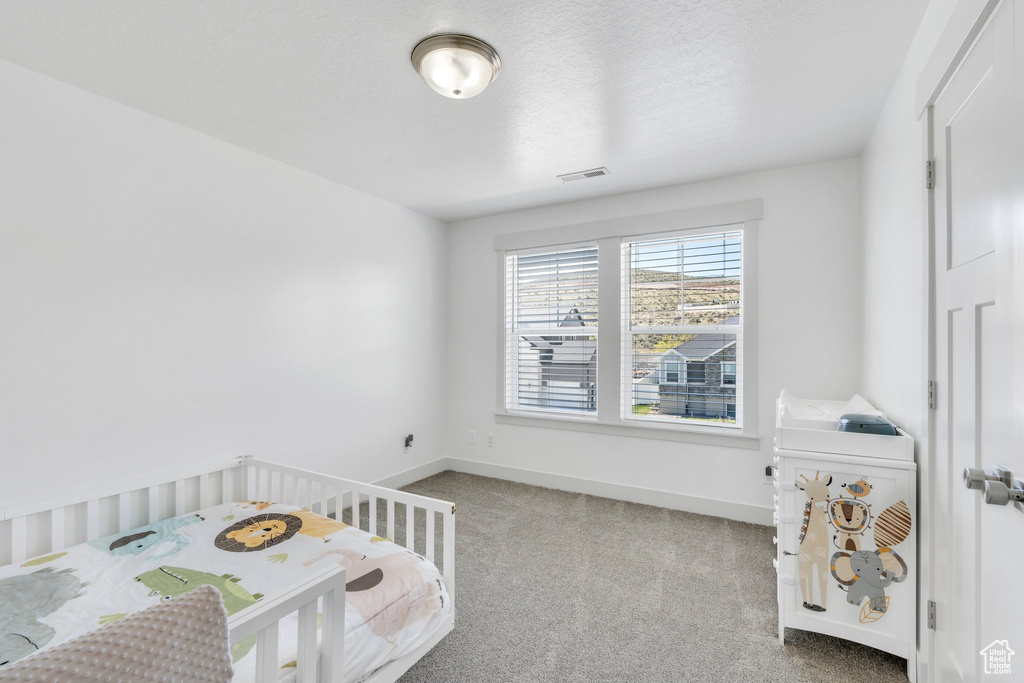 Bedroom with baseboards, a crib, visible vents, and carpet floors