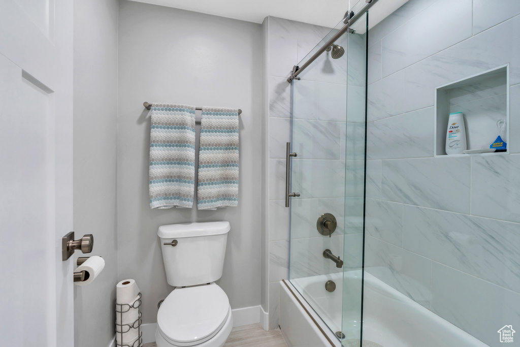 Full bathroom featuring toilet, shower / bath combination with glass door, and baseboards