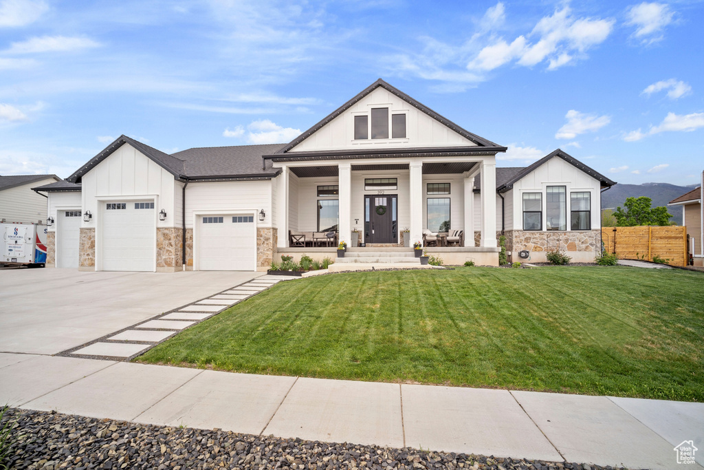 View of front of home featuring board and batten siding, a porch, stone siding, a garage, and driveway