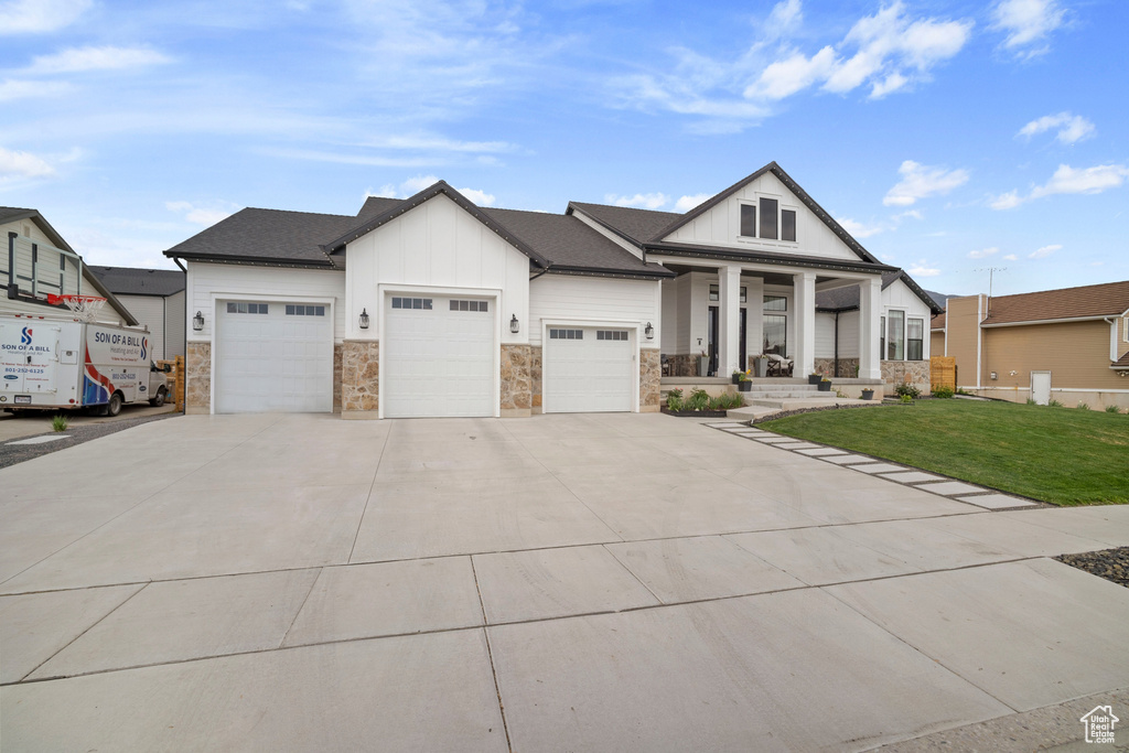 View of front of house with a porch, an attached garage, board and batten siding, a front lawn, and concrete driveway