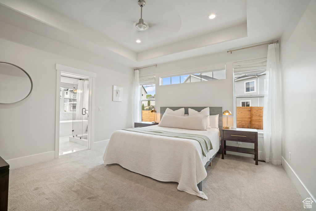 Bedroom with ensuite bath, recessed lighting, light carpet, a raised ceiling, and baseboards
