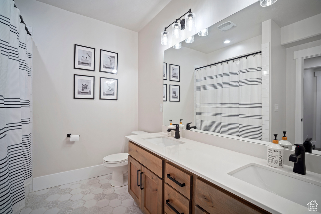 Full bath with a sink, double vanity, toilet, and baseboards