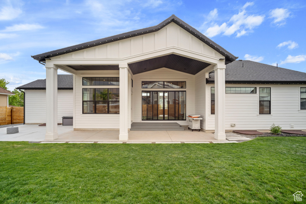 Back of property with a yard, board and batten siding, fence, a patio area, and roof with shingles