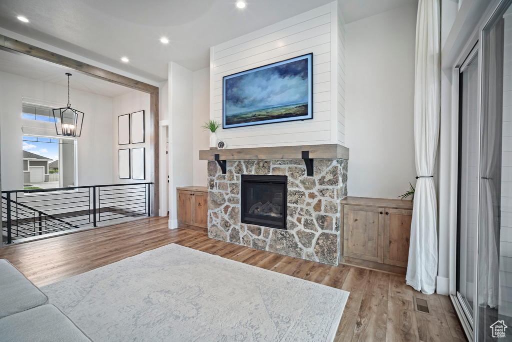 Living room featuring wood finished floors, a chandelier, recessed lighting, and a stone fireplace