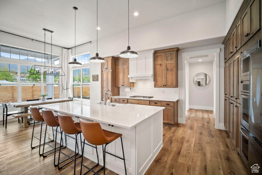 Kitchen with baseboards, a spacious island, backsplash, gas stovetop, and light countertops