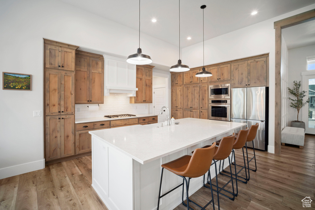 Kitchen with appliances with stainless steel finishes, decorative backsplash, brown cabinetry, and light wood-style floors