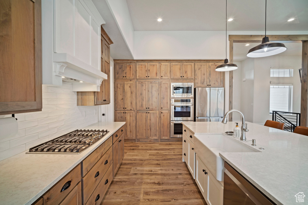 Kitchen with a sink, stainless steel appliances, decorative light fixtures, backsplash, and light wood-style floors