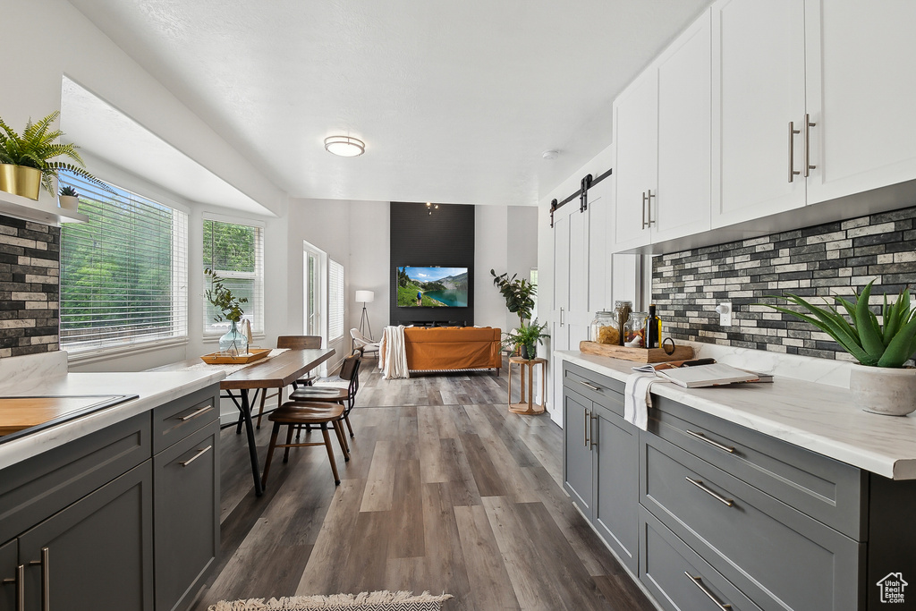 Kitchen featuring gray cabinets, a barn door, light countertops, decorative backsplash, and dark wood-style floors