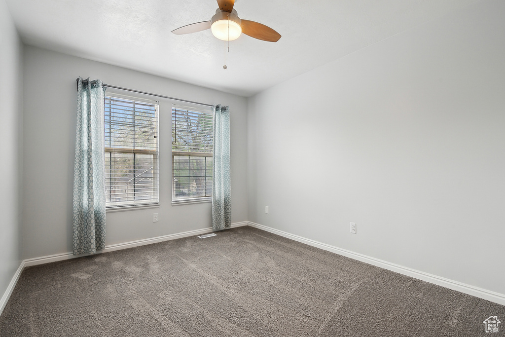 Unfurnished room with a ceiling fan, dark carpet, baseboards, and visible vents