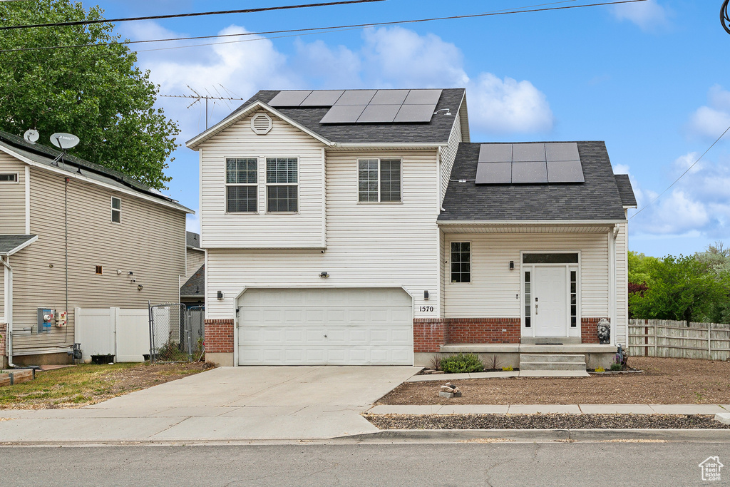 Traditional home featuring fence, brick siding, driveway, solar panels, and a shingled roof