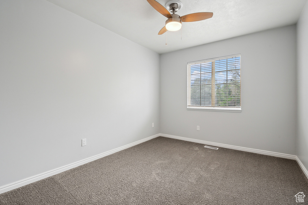 Empty room with ceiling fan, baseboards, visible vents, and dark carpet