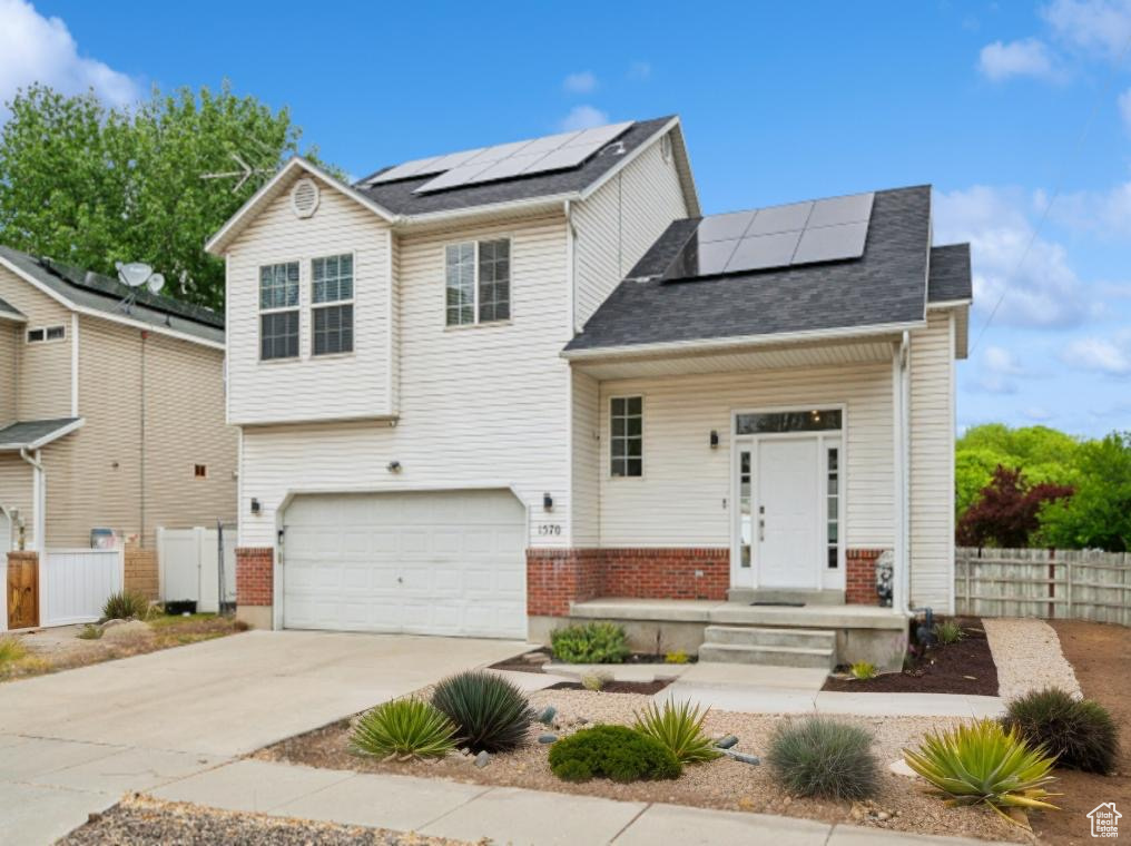 View of front of property with roof mounted solar panels, fence, an attached garage, and driveway