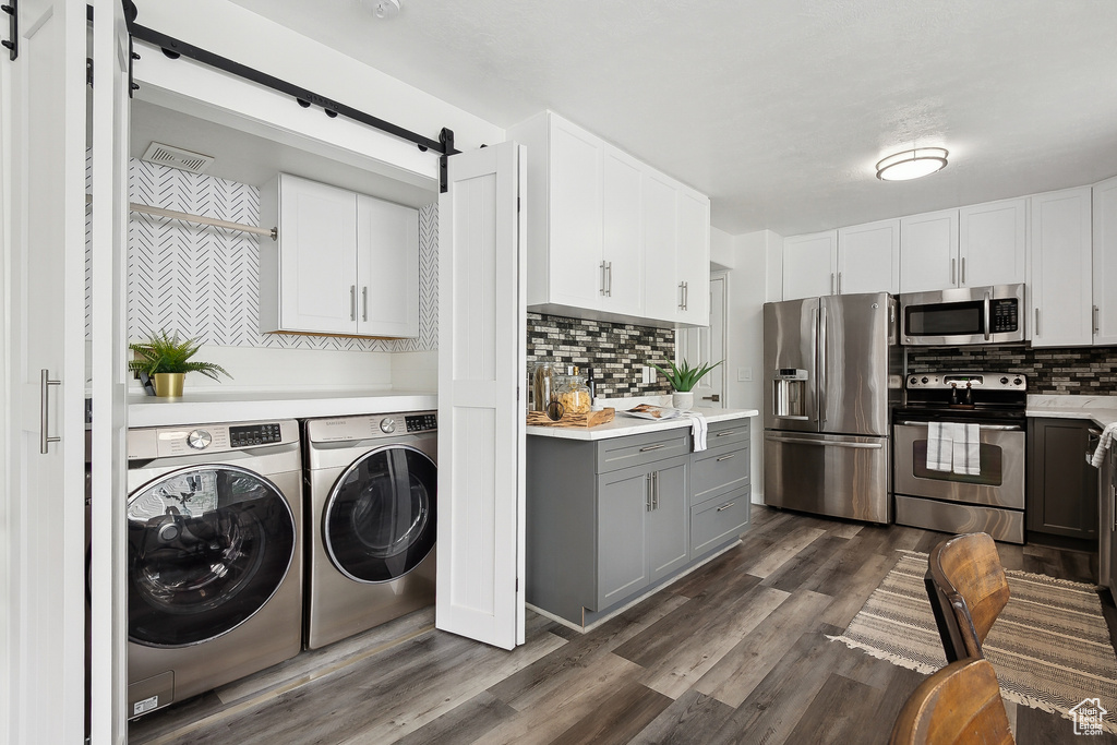 Clothes washing area featuring washing machine and clothes dryer, dark wood-style flooring, a barn door, and laundry area