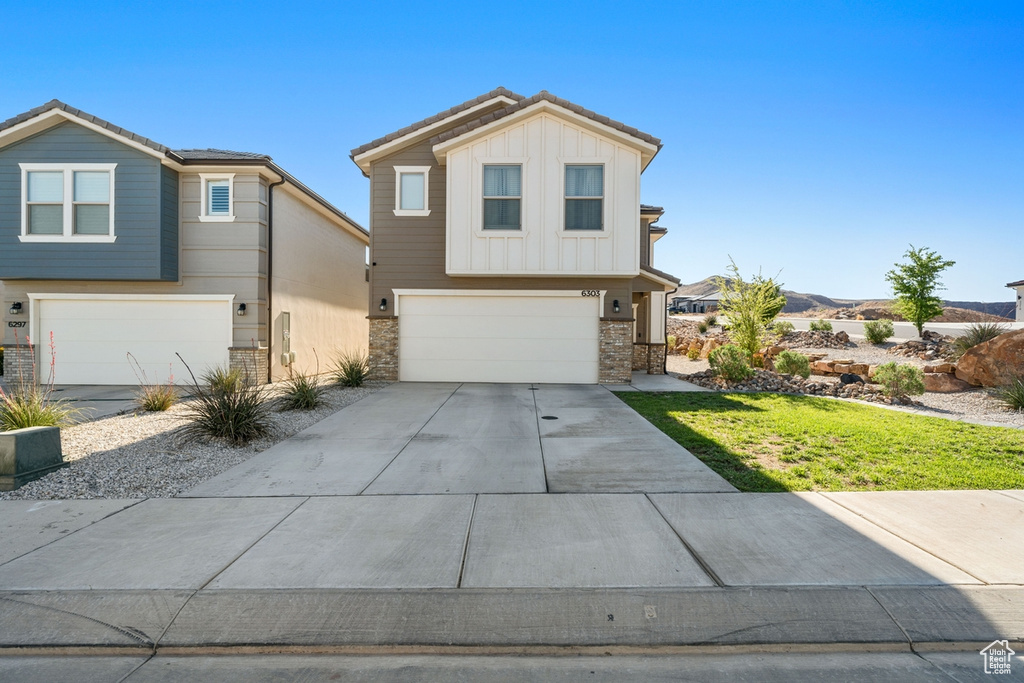 Traditional home with concrete driveway, a garage, stone siding, and board and batten siding