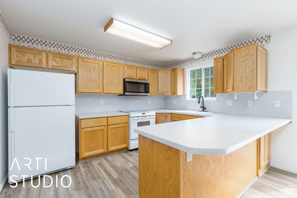 Kitchen with white appliances, light wood finished floors, light countertops, a sink, and a peninsula