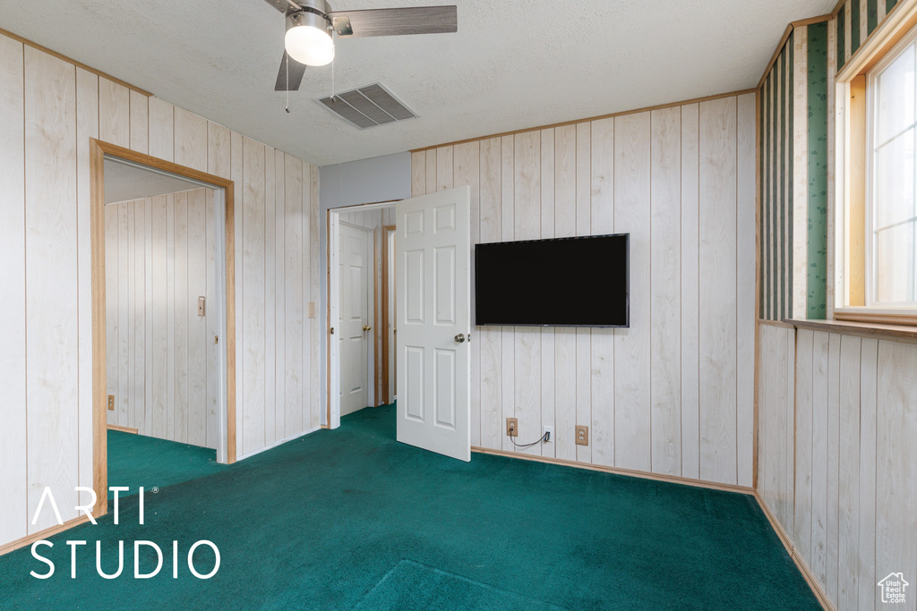 Unfurnished bedroom with wooden walls, carpet floors, multiple windows, and ceiling fan