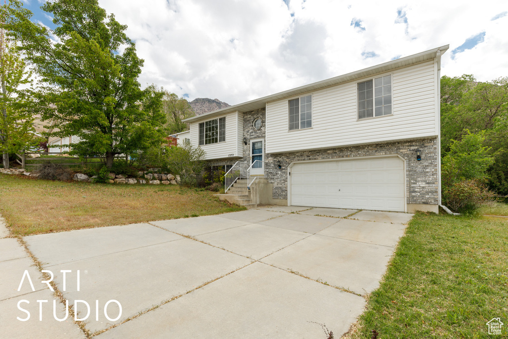 Bi-level home with an attached garage, concrete driveway, and a front lawn