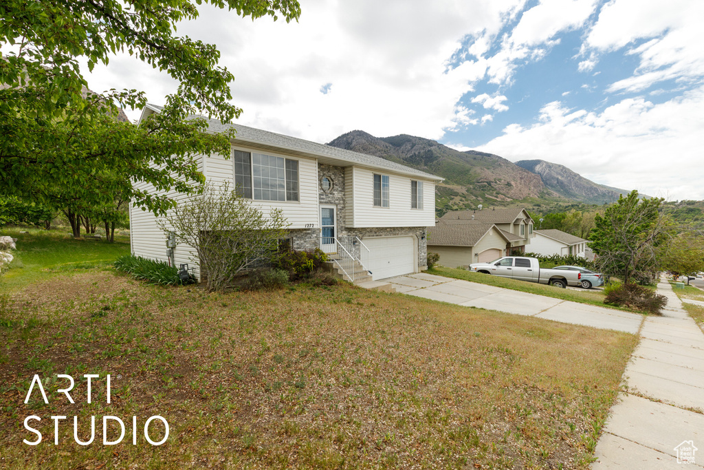 Raised ranch featuring a mountain view, concrete driveway, an attached garage, and a front yard