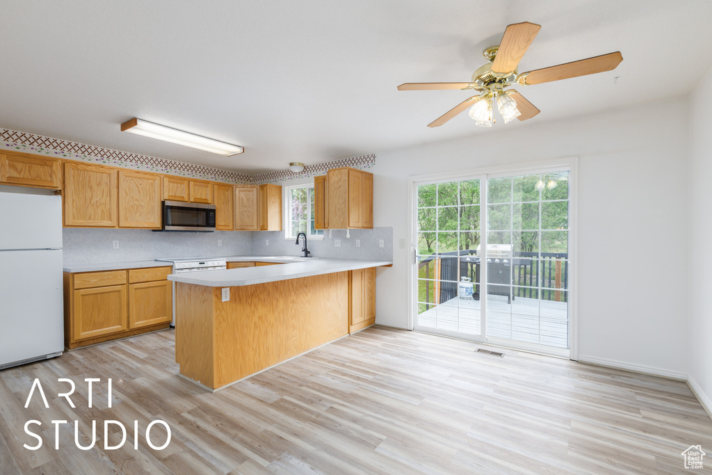 Kitchen with freestanding refrigerator, stainless steel microwave, light countertops, and light wood-style floors
