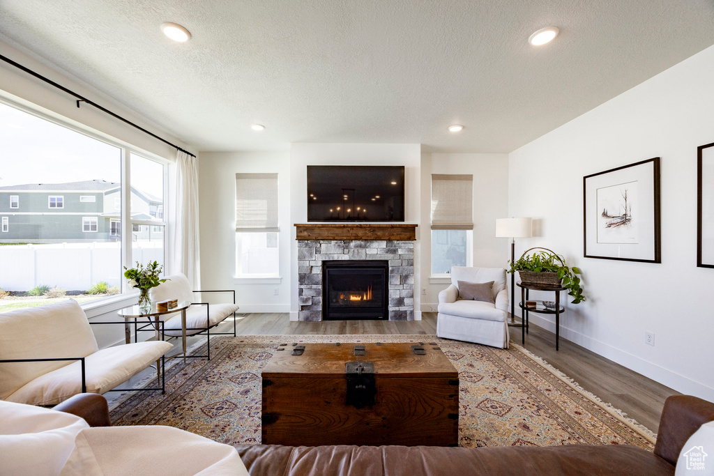 Living area with wood finished floors, baseboards, a stone fireplace, recessed lighting, and a textured ceiling